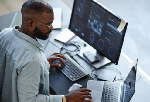 istockphoto-1435220822-612x612 Minimal high angle view at African American software developer working with computers and data systems in office